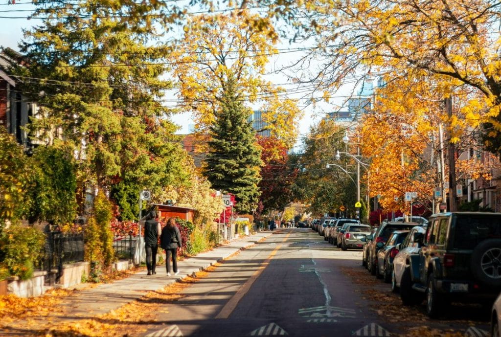 street in Leslieville, Toronto, showing fall leaves, a couple walking and cars parked along the street