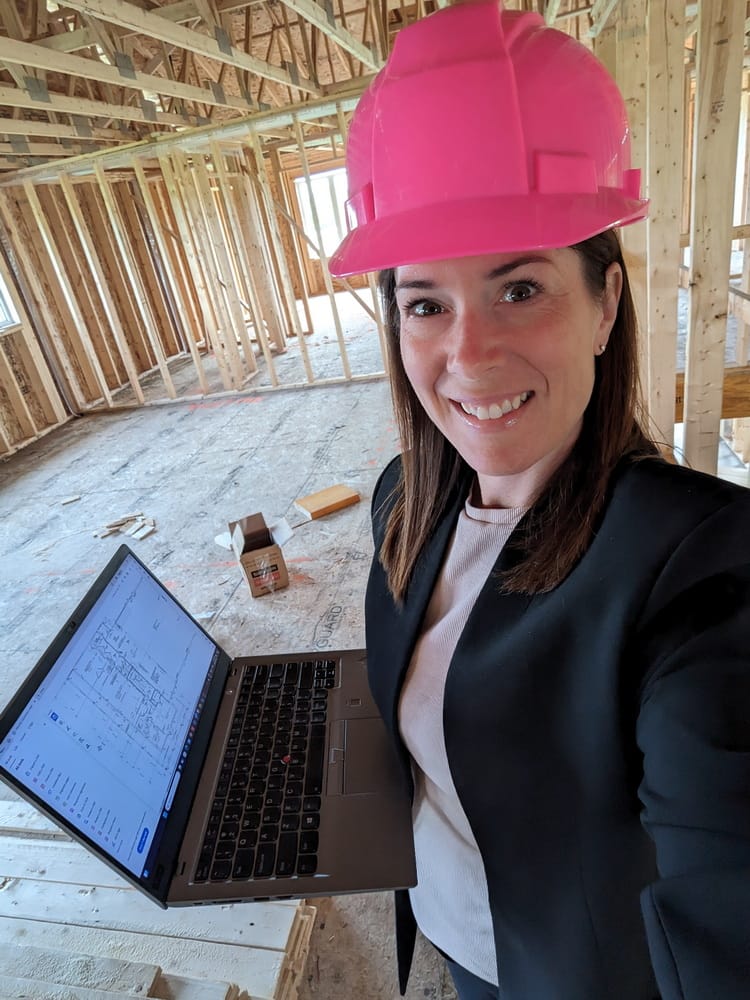 woman in a pink hard hat with a laptop at a home under construction