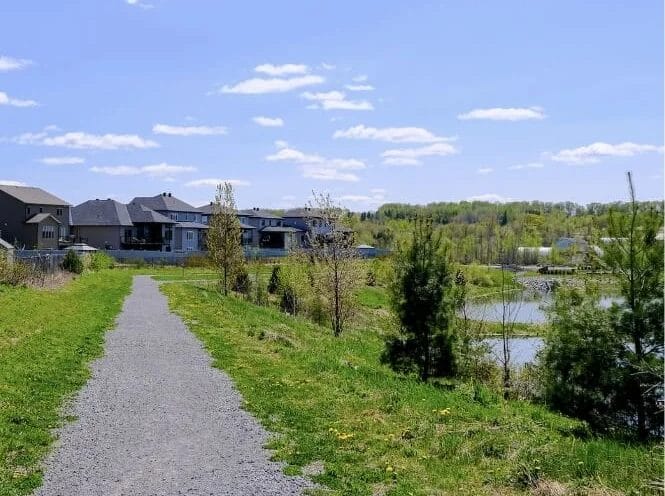 a gravel path beside a stormwater pond with new homes in the background in Clarence-Rockland
