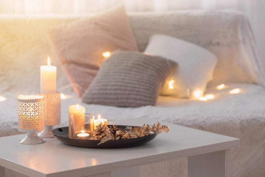 cosy for winter Christmas decoration with burning candles on white table against the background of sofa with plaids and pillows. 