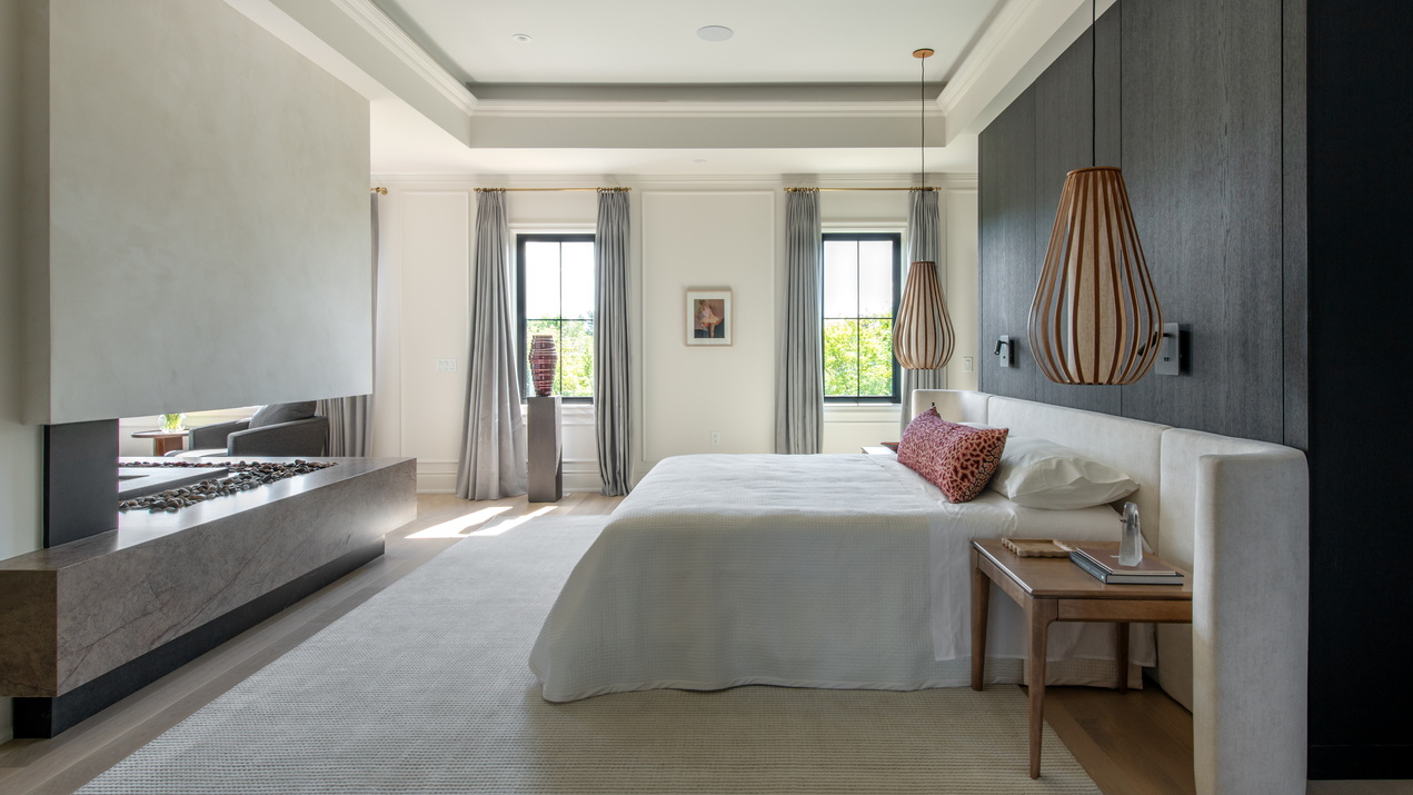 primary bedroom in the 2026 Minto dream home, showing the sleeping area with cove ceiling and part of the L-shaped look-through fireplace
