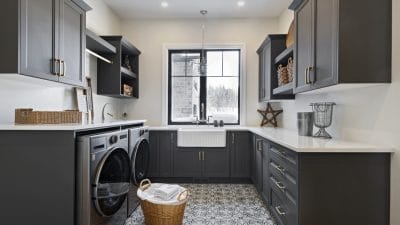 photo of a laundry room with dark cabinets on three walls, a white apron sink, a window and geometric tile on the floor