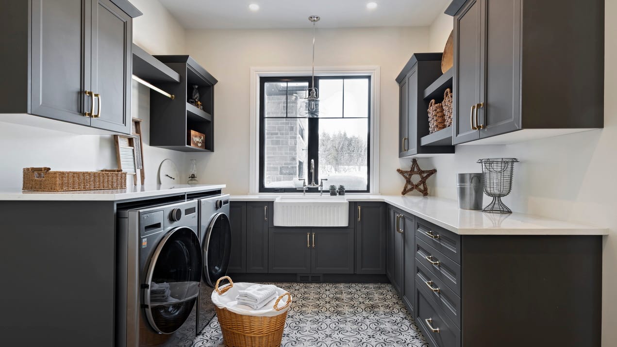 photo of a laundry room with dark cabinets on three walls, a white apron sink, a window and geometric tile on the floor