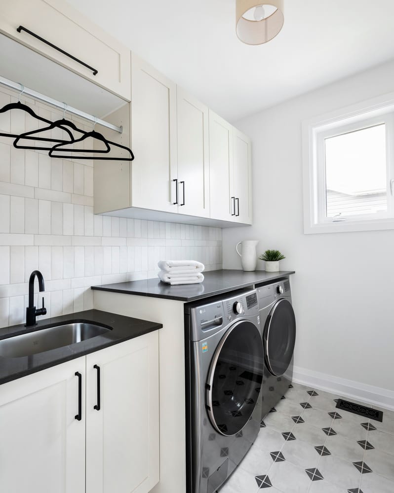laundry room with white cabinets, a sink, black counters, stainless-steel washer and dryer and geometric tile floor