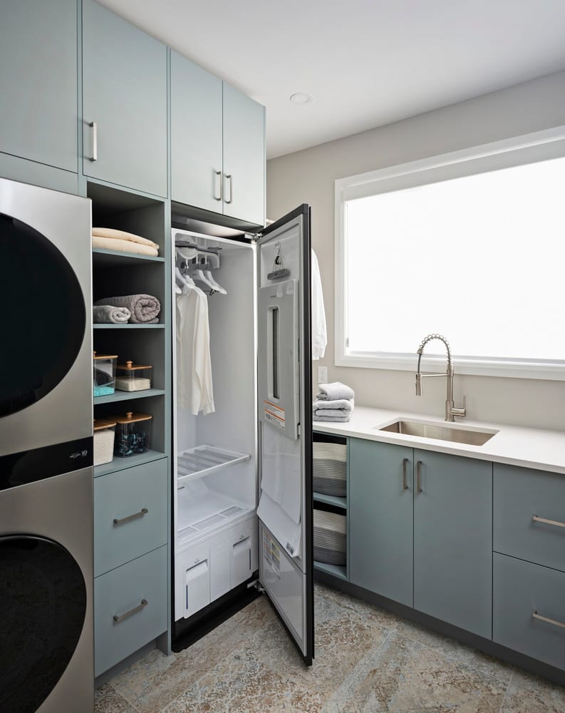 laundry room with floor-to-ceiling cabinetry that includes a steam cabinet, stacked washer and dryer and sink