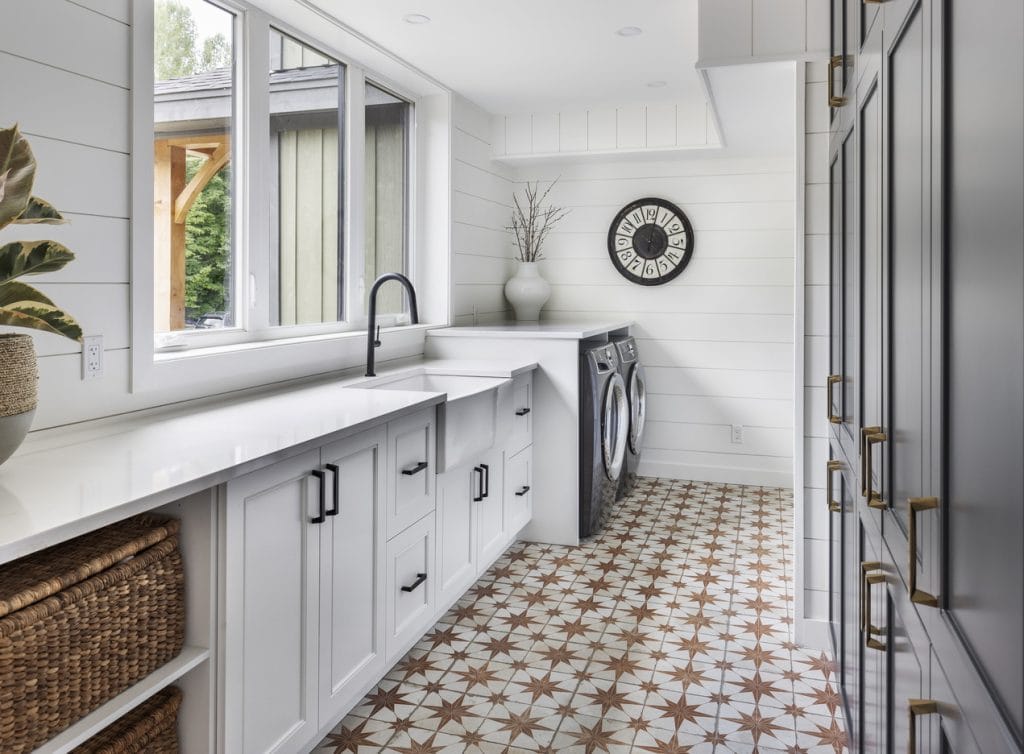 modern farmhouse style laundry room with shiplap, shaker cabinets and an apron sink paired with geometric floor tile