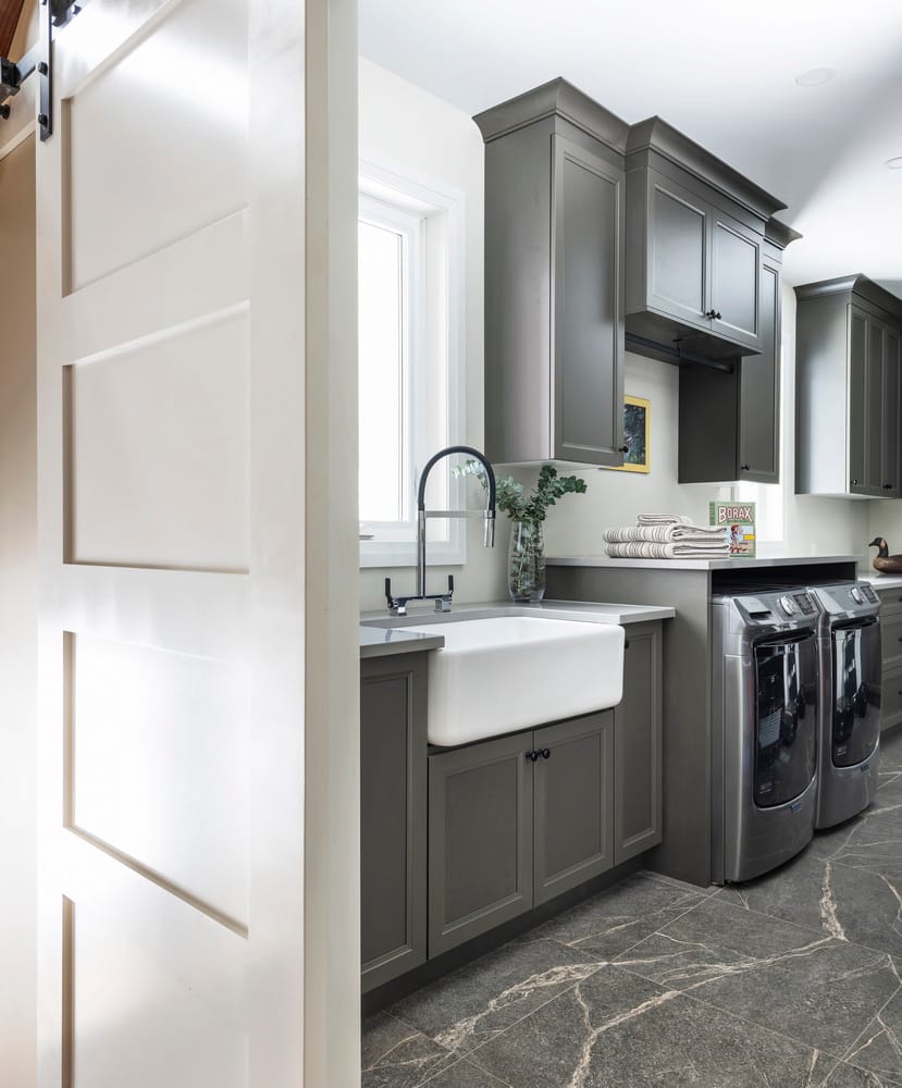 laundry room with barn door, grey cabinets, apron sink and grey marbled tile flooring