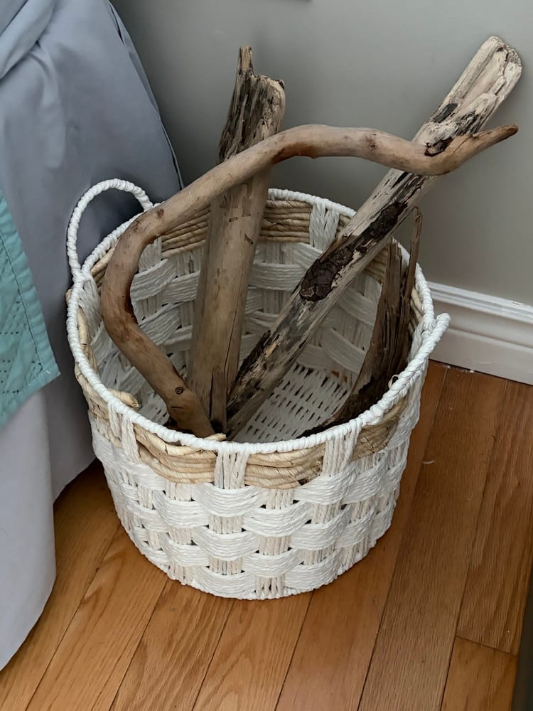 pieces of driftwood in a white wicker basket beside a bed