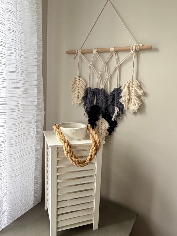 macrame artwork with feathers attached and a white hurricane lantern