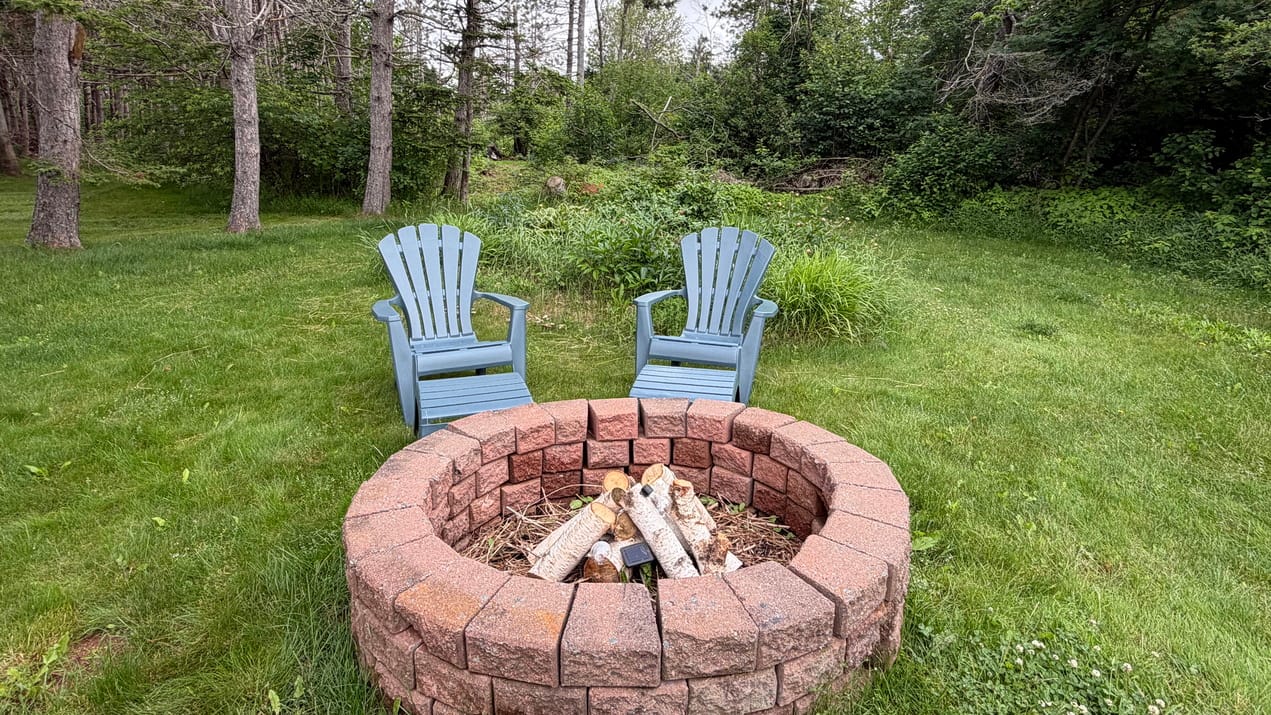 Muskoka or adirondack chairs by a brick firepit in a backyard