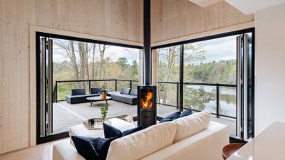 : inside a cabin made from cross-laminated timber, looking our the corner picture window, which has a woodstove at the corner