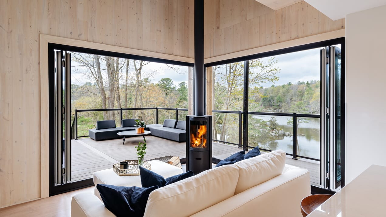 : inside a cabin made from cross-laminated timber, looking our the corner picture window, which has a woodstove at the corner
