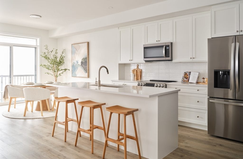 kitchen and dining area of the open-concept Dorchester three-storey townhome model by Urbandale at Riverside South featuring an all-white kitchen and island with three wood stools