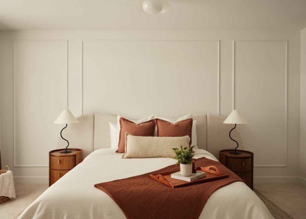 primary bedroom of the Discovery townhome model by Urbandale at Kanata Lakes, featuring deep rose accent pillows and throw and moulding on the wall for a panelled look