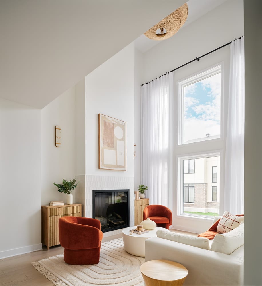 two-storey living room in the Endeavour townhome model by Urbandale at Riverside South with a built-in electric fireplace white sofa and burgundy bucket chairs